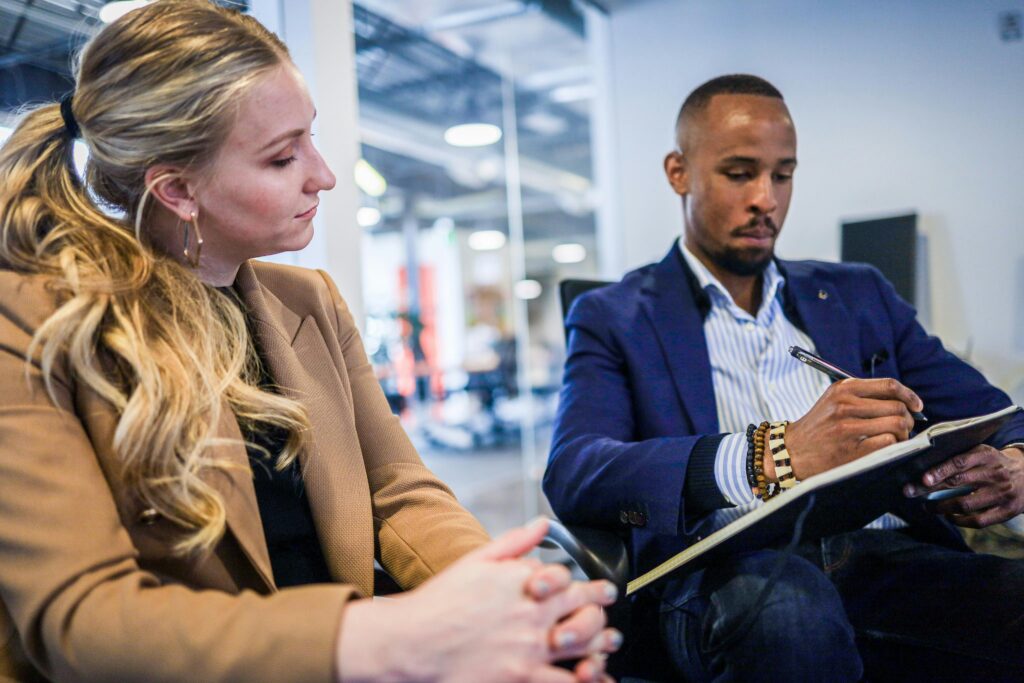 Adult female and adult male in business attire holding a notebook and pen explaining a project